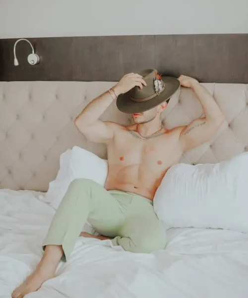 a-man-in-green-pants-and-a-hat-sitting-on-a-bed-27251761